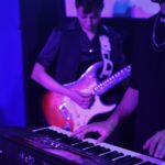 Antonella Vitanza tocando la guitarra eléctrica junto al tecladista de Quiero Cumbia durante un show en vivo.