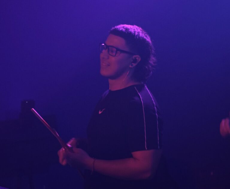 Percusionista de Quiero Cumbia tocando en vivo bajo luces violetas