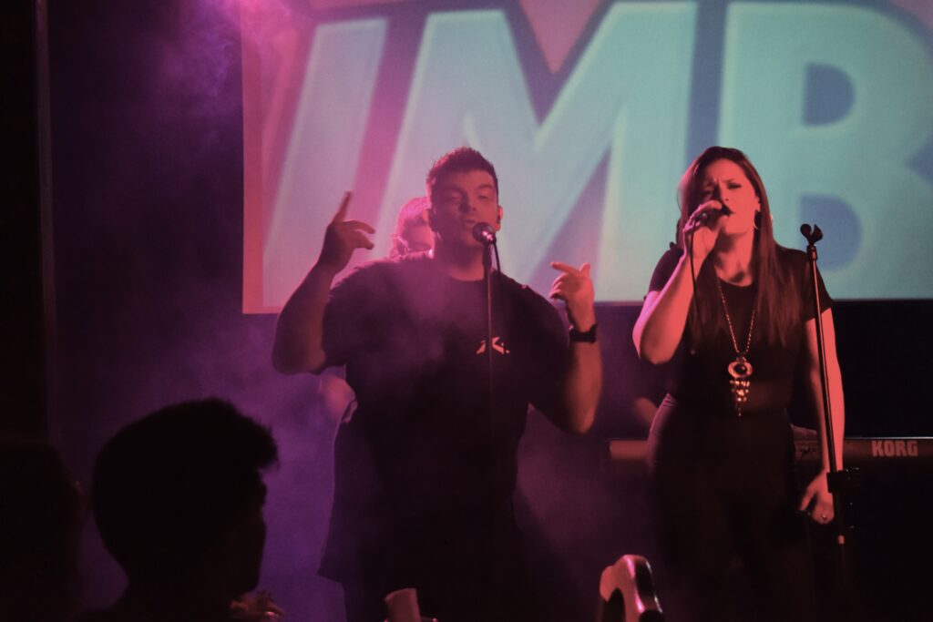 Euge Luján y Georgina Otero cantando juntos en un show en vivo de Quiero Cumbia, con luces y pantalla de fondo