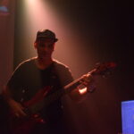 Emanuel Aloise tocando el bajo en vivo con la banda Quiero Cumbia bajo luces cálidas