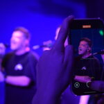 Cantante de Quiero Cumbia grabado por un celular durante un show en vivo, con el escenario desenfocado de fondo